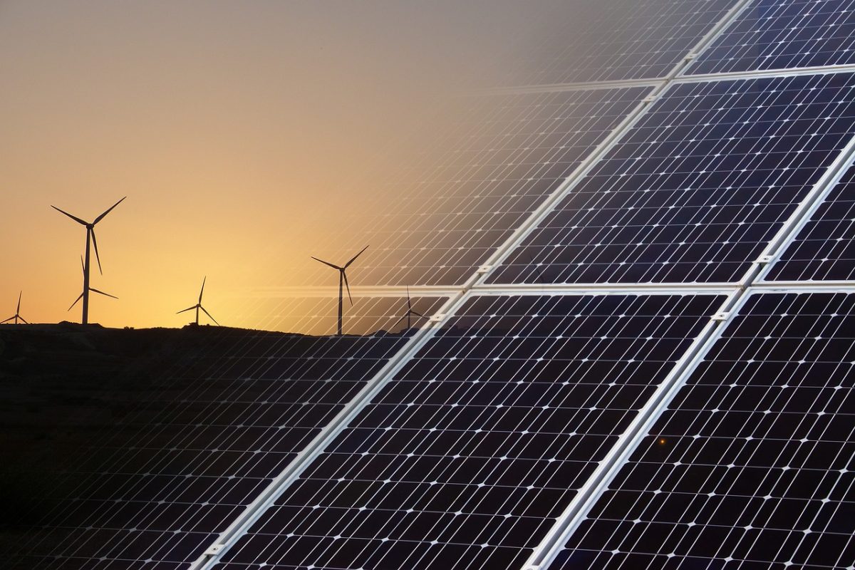 A landscape view of Green energy sources with wind turbines in the background and solar panels in the foreground at sunset.